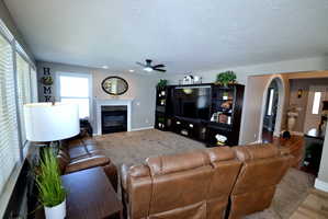 Living area featuring arched walkways, a premium fireplace, a ceiling fan, a textured ceiling, and wood finished floors