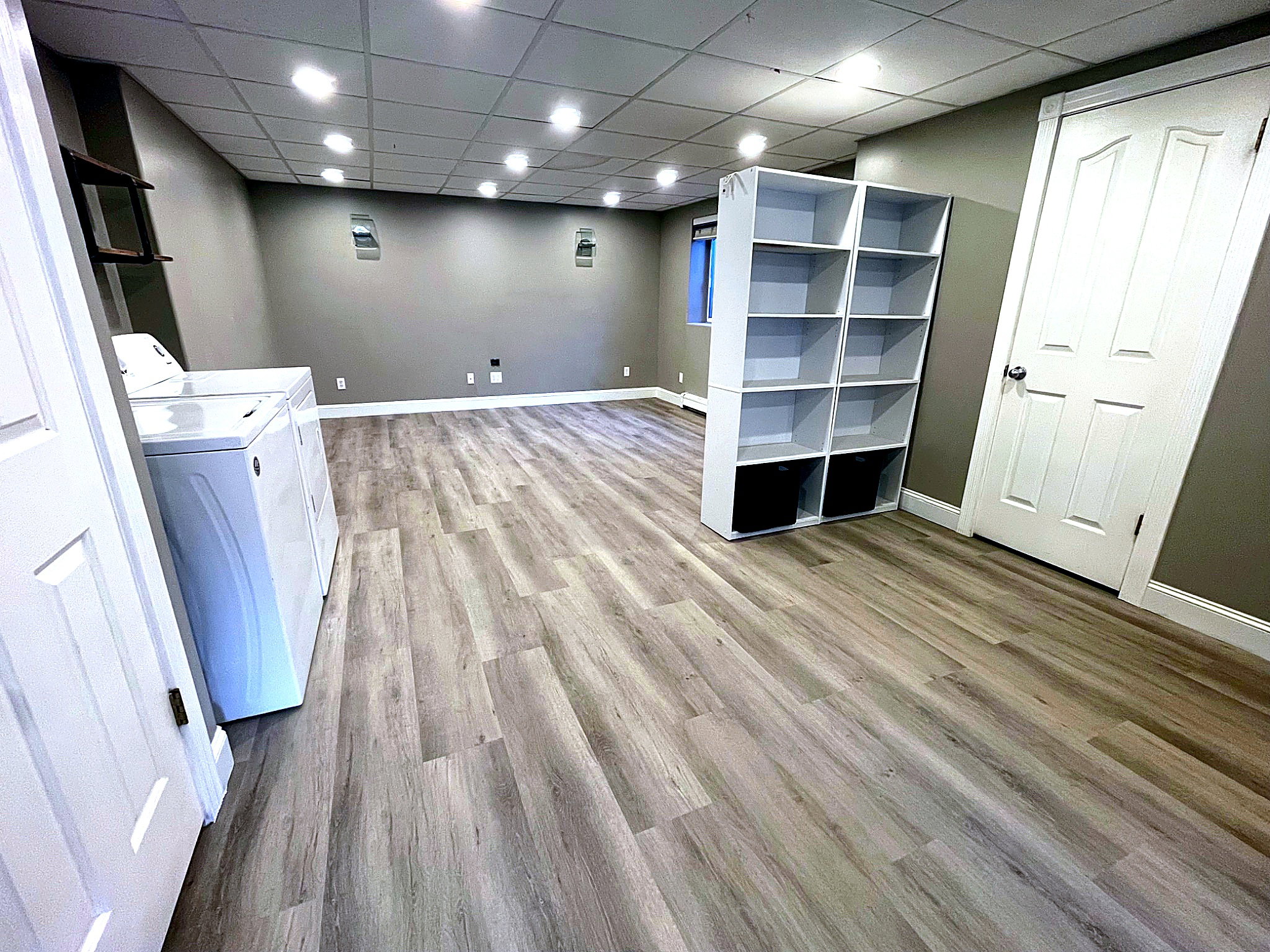 Finished below grade area with a paneled ceiling, light wood-type flooring, washer and clothes dryer, and recessed lighting