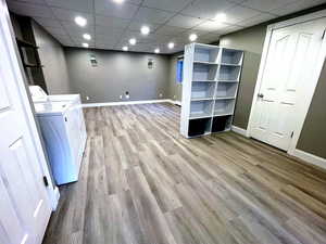 Finished below grade area with a paneled ceiling, light wood-type flooring, washer and clothes dryer, and recessed lighting