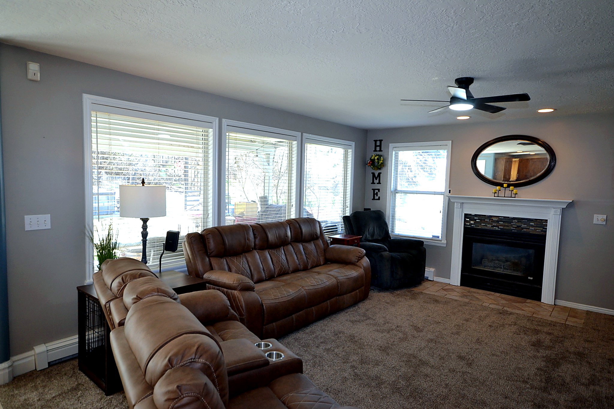 Living room featuring carpet floors, a ceiling fan, a baseboard radiator, a glass covered fireplace, and a textured ceiling