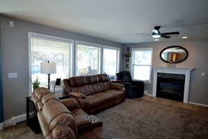 Living room featuring carpet floors, a ceiling fan, a baseboard radiator, a glass covered fireplace, and a textured ceiling