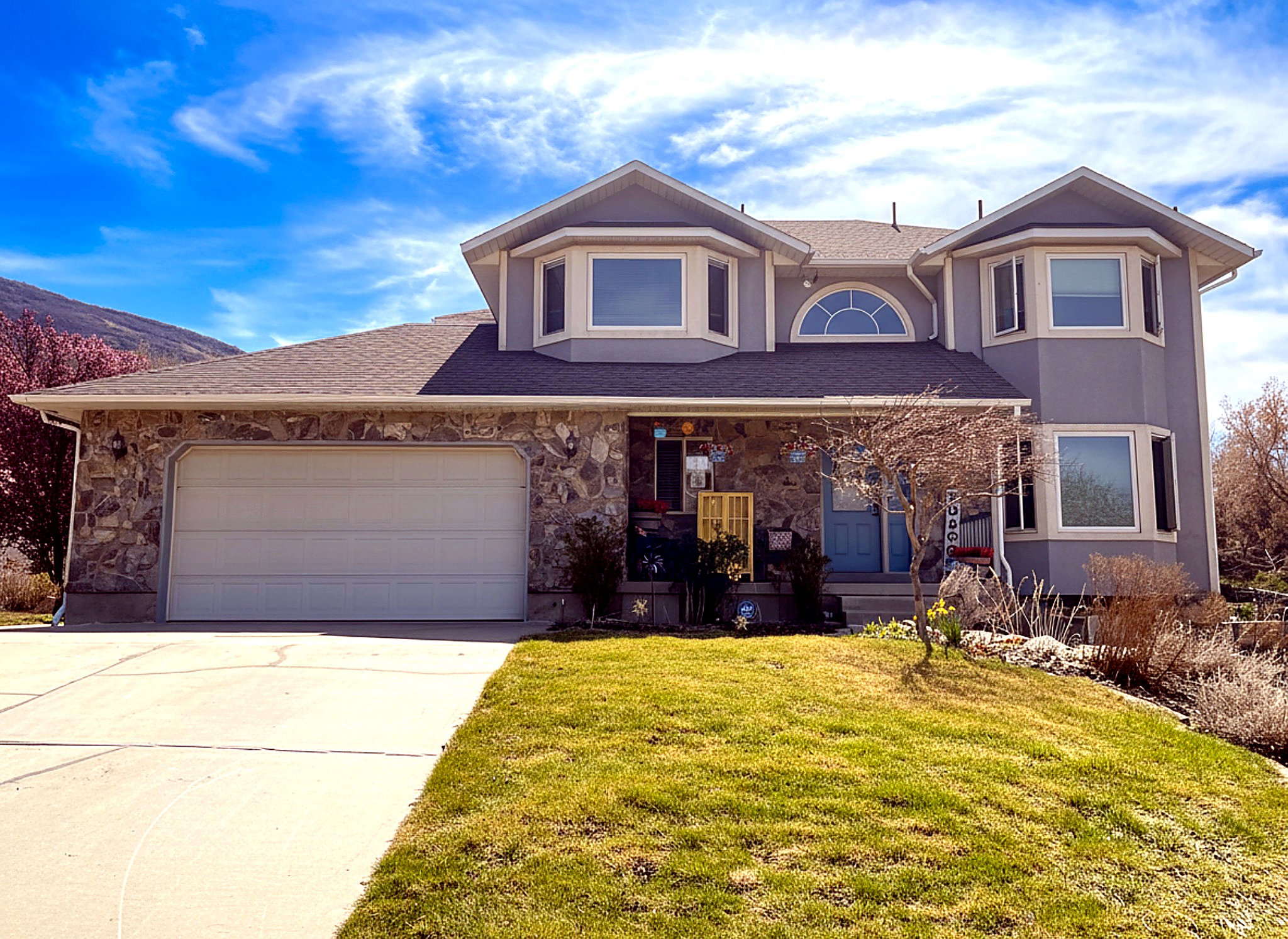 View of front of home featuring covered porch, stone siding, concrete driveway, and a front yard