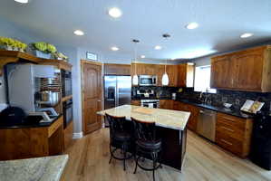 Kitchen featuring a kitchen breakfast bar, decorative light fixtures, stainless steel appliances, a center island, and light wood-style floors
