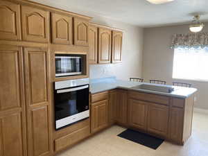 Kitchen featuring a peninsula, wall oven, light countertops, stainless steel microwave, and a breakfast bar