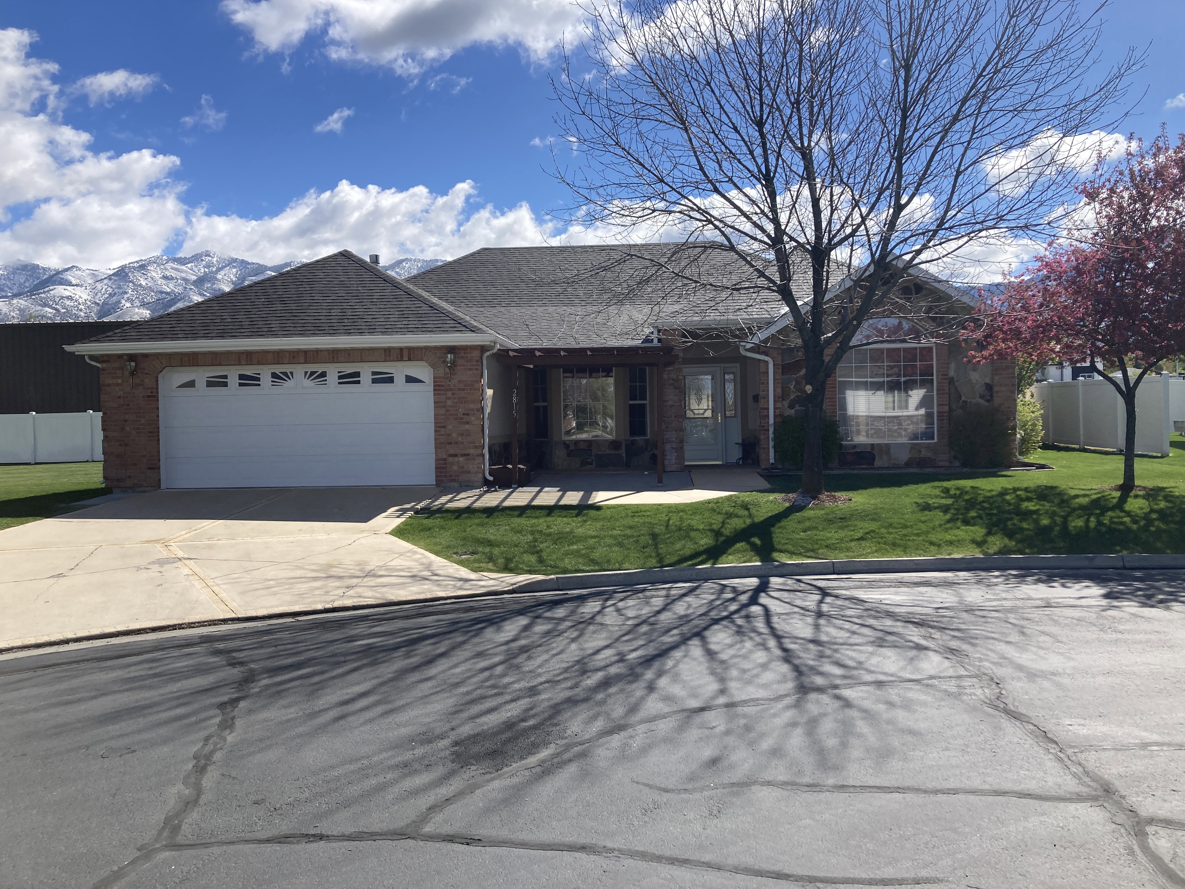 Single story home with brick siding, an attached garage, a shingled roof, concrete driveway, and a patio area