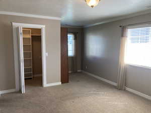 Unfurnished bedroom with a walk in closet, light colored carpet, crown molding, and a textured ceiling