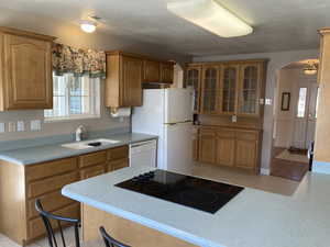 Kitchen featuring arched walkways, glass fronted cabinets, wood finish cabinets, light countertops, and a textured ceiling