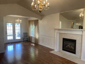 Unfurnished living room featuring arched walkways, a chandelier, dark wood finished floors, a decorative wall, and wainscoting