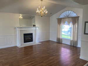 Unfurnished living room with dark wood-style floors, suspended lighting, a fireplace, lofted ceiling, and wainscoting