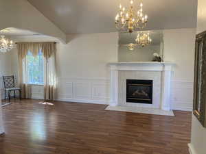 Unfurnished living room with suspended lighting, dark wood-style flooring, a decorative wall, wainscoting, and a tile fireplace
