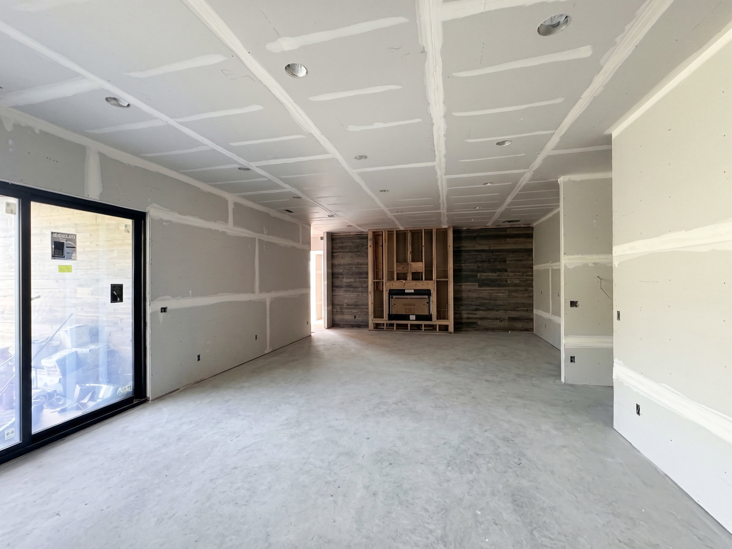 Spacious interior offering an open layout, recessed lighting, concrete flooring, and a fireplace framed by wood-paneled walls