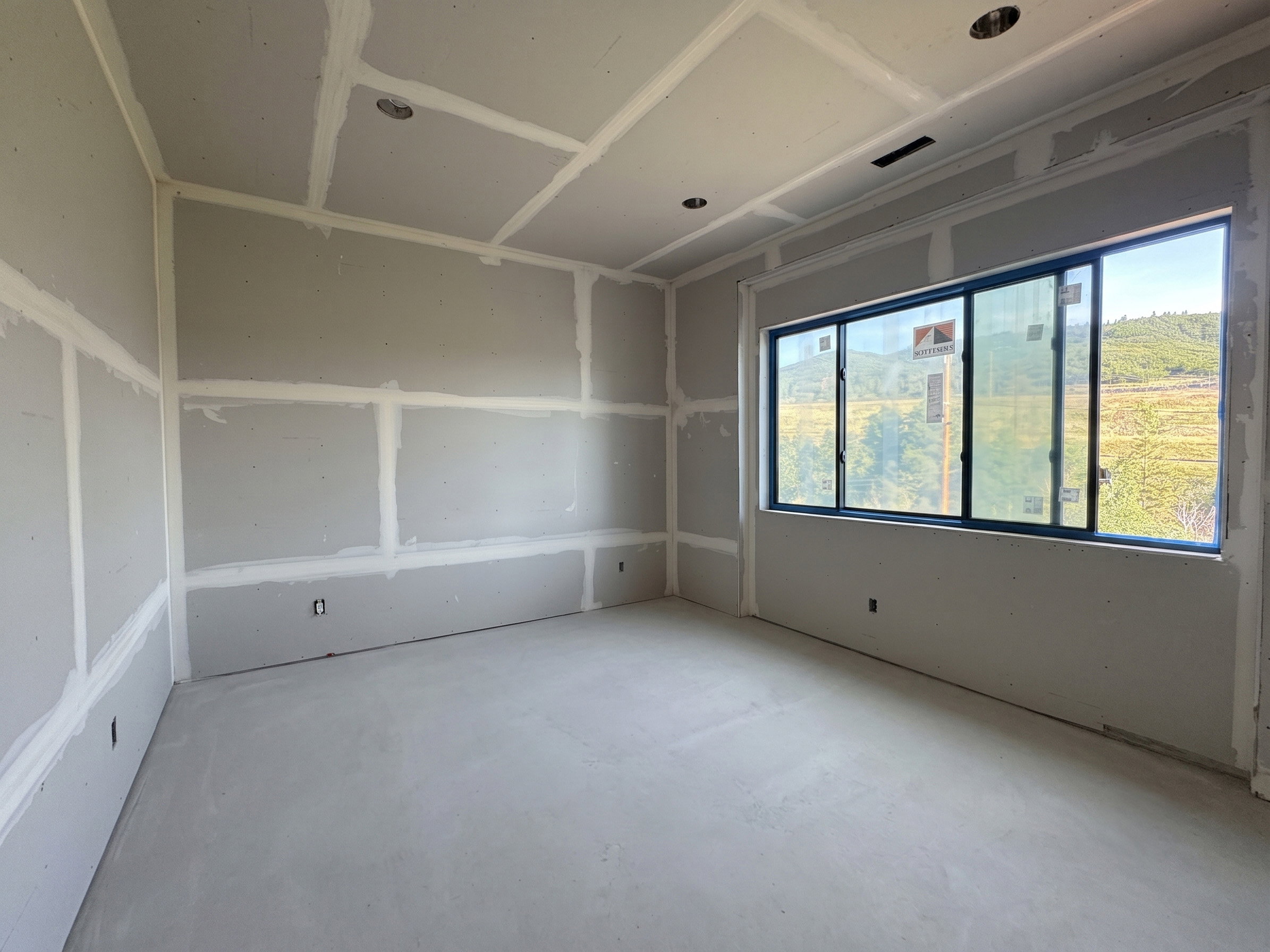 Unfinished interior space featuring a large window with multiple panes, recessed ceiling lighting, and a visible exterior landscape