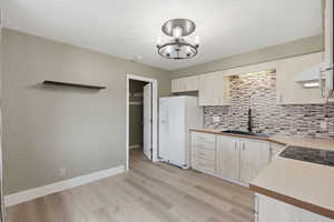Kitchen featuring light countertops, light wood-type flooring, exhaust hood, white refrigerator with ice dispenser, and suspended lighting