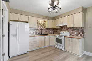 Kitchen with light wood finish cabinetry, white appliances, and light countertops