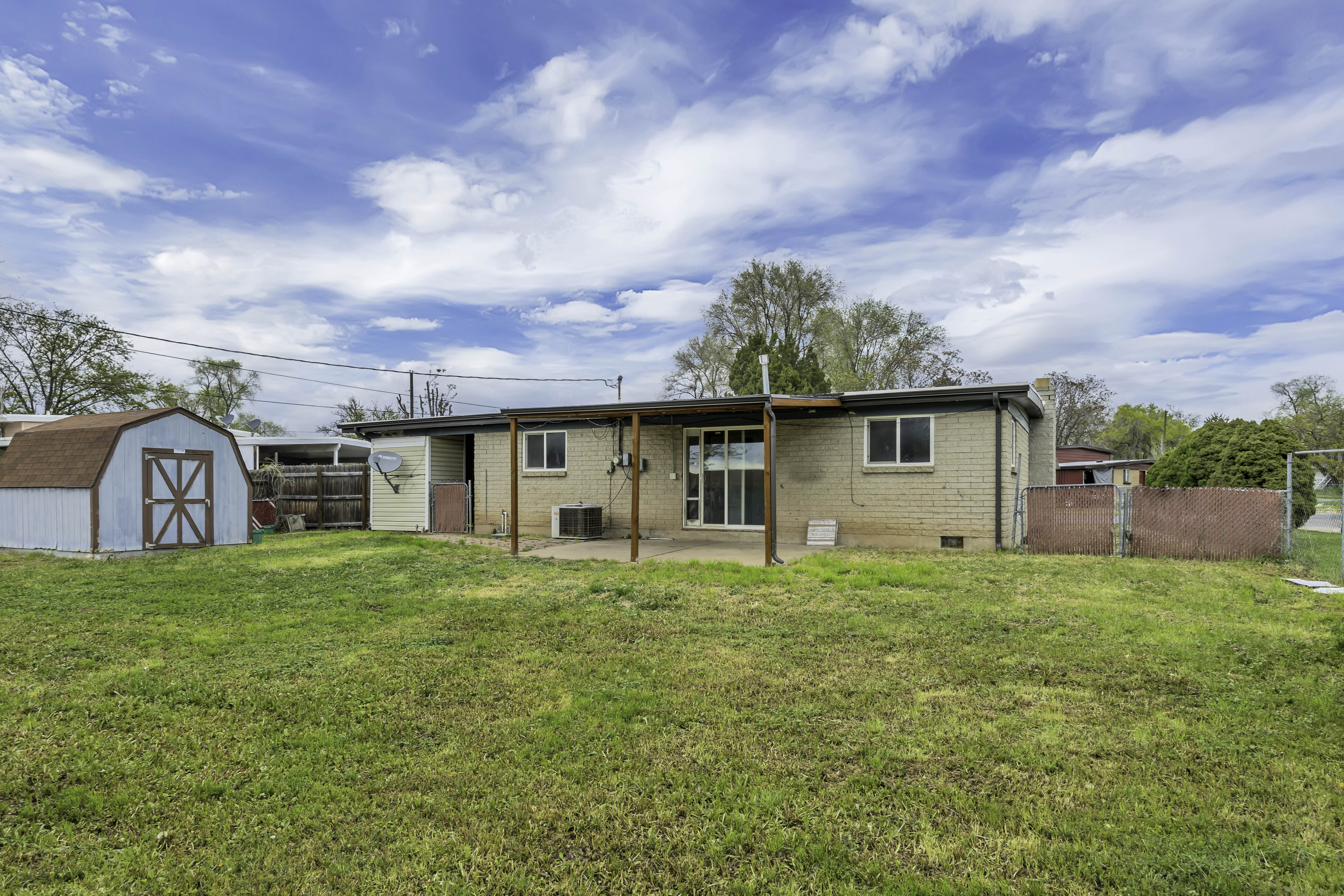 Back of property featuring brick siding, a patio area, a fenced backyard, and a shed