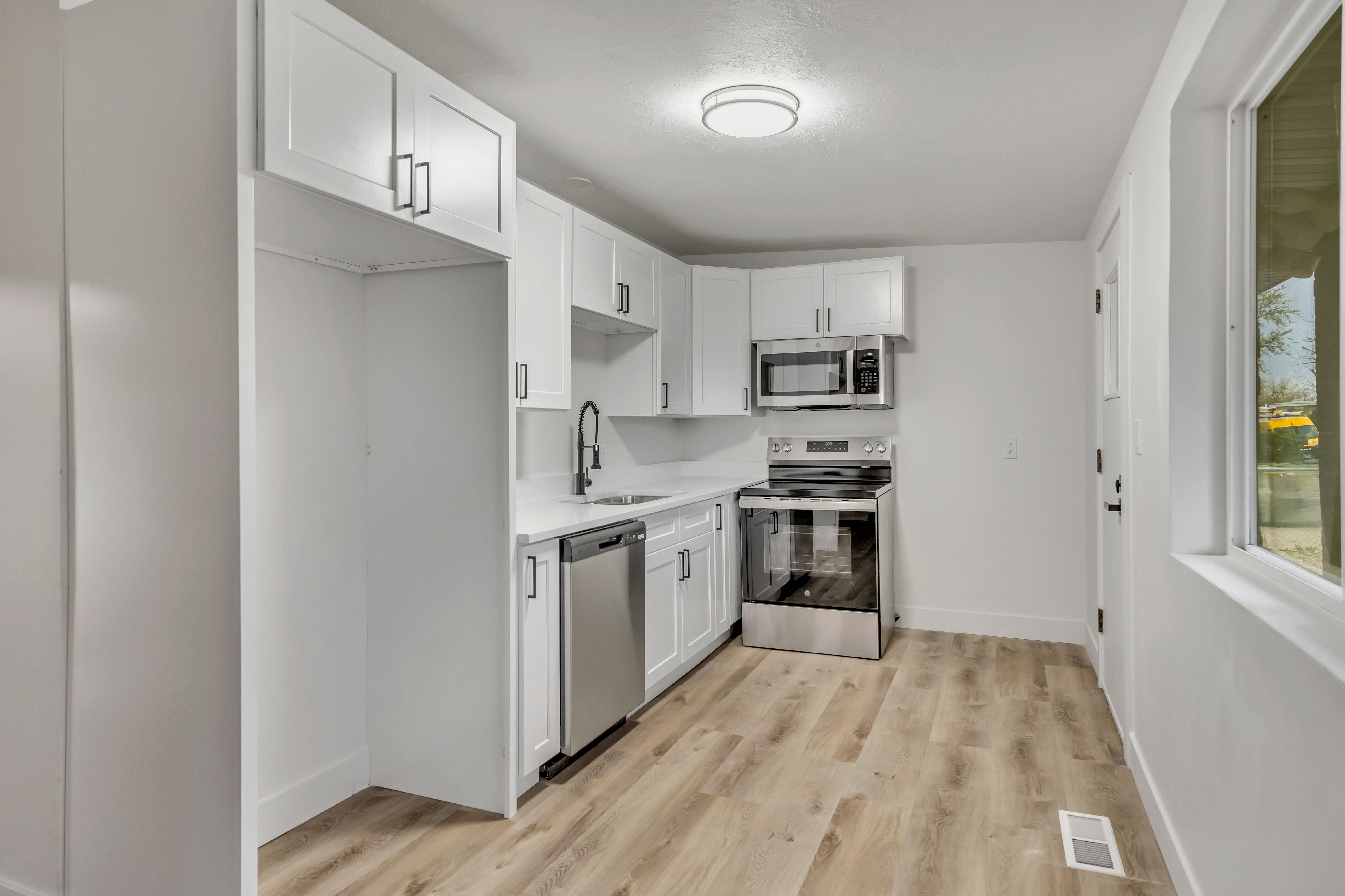 Kitchen with stainless steel appliances, white cabinetry, and light wood-style flooring