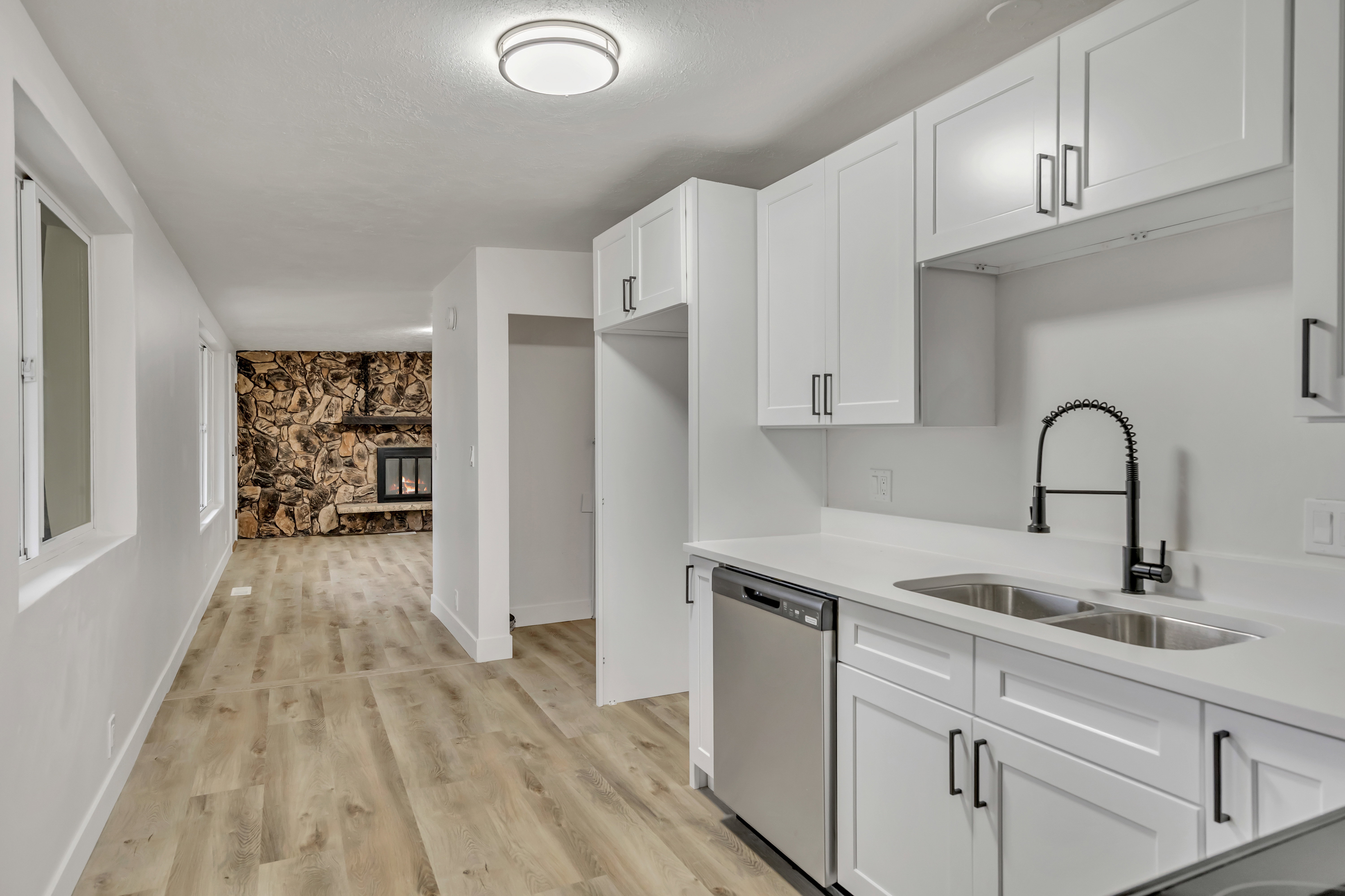 Kitchen featuring white cabinets, a fireplace, stainless steel dishwasher, light wood-style floors, and light stone counters
