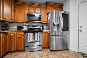 Kitchen with stainless steel appliances, wood finish cabinets, light stone counters, and light tile patterned floors