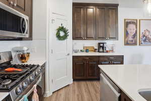 Kitchen featuring stainless steel appliances, dark wood finish cabinetry, light wood finished floors, light stone countertops, and tasteful backsplash