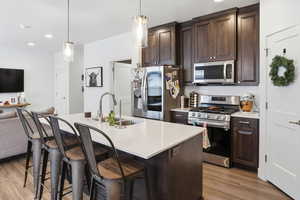 Kitchen featuring dark wood finish cabinetry, open floor plan, stainless steel appliances, a breakfast bar, and an island with sink