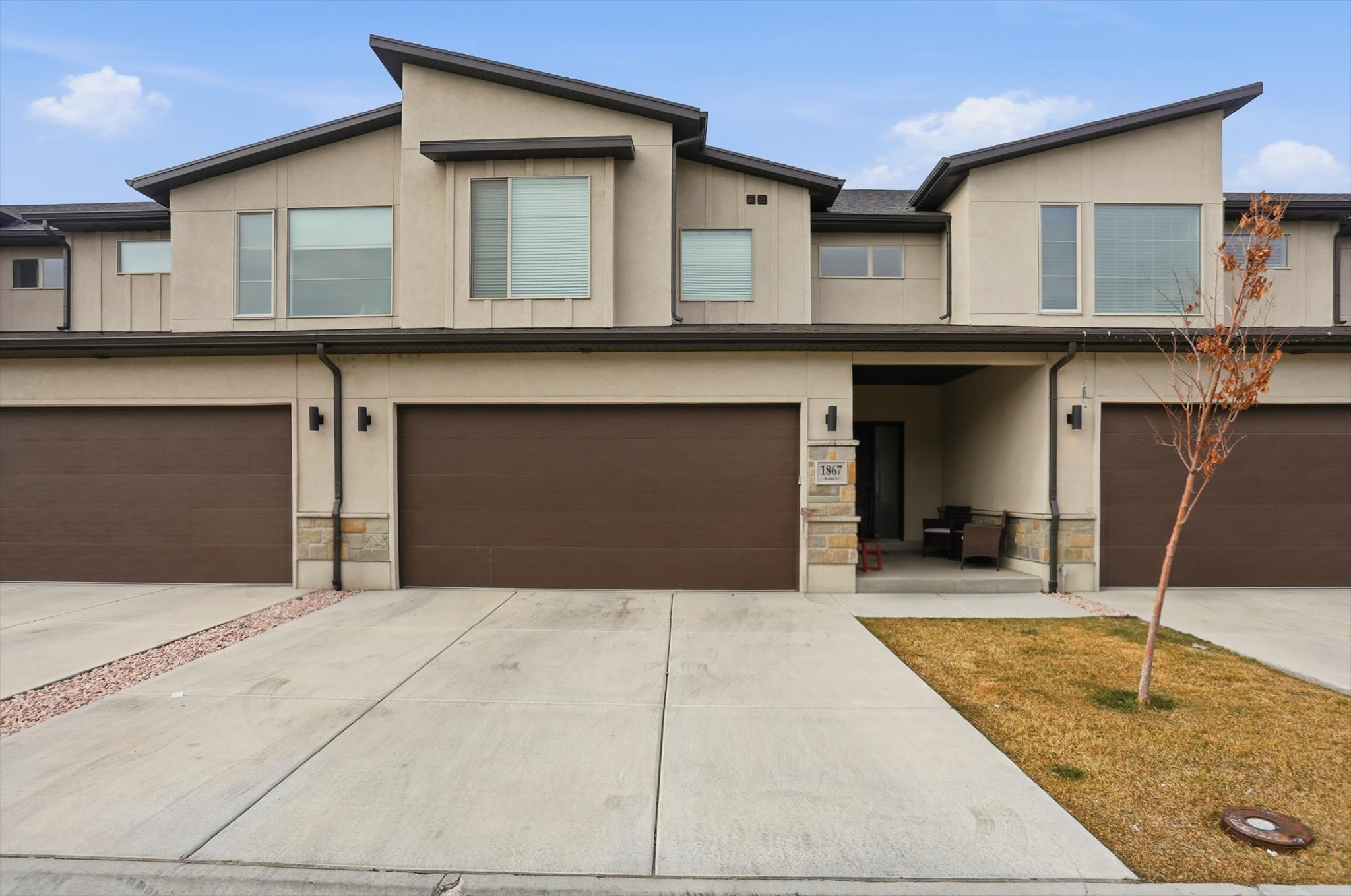 Contemporary home with stone siding, an attached garage, stucco siding, driveway, and covered porch