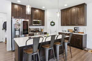 Kitchen featuring dark wood finish cabinetry, a breakfast bar, an island with sink, pendant lighting, and stainless steel appliances