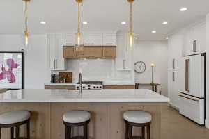 Kitchen with a kitchen breakfast bar, dual tone cabinets, white appliances, tasteful backsplash, and light wood-type flooring