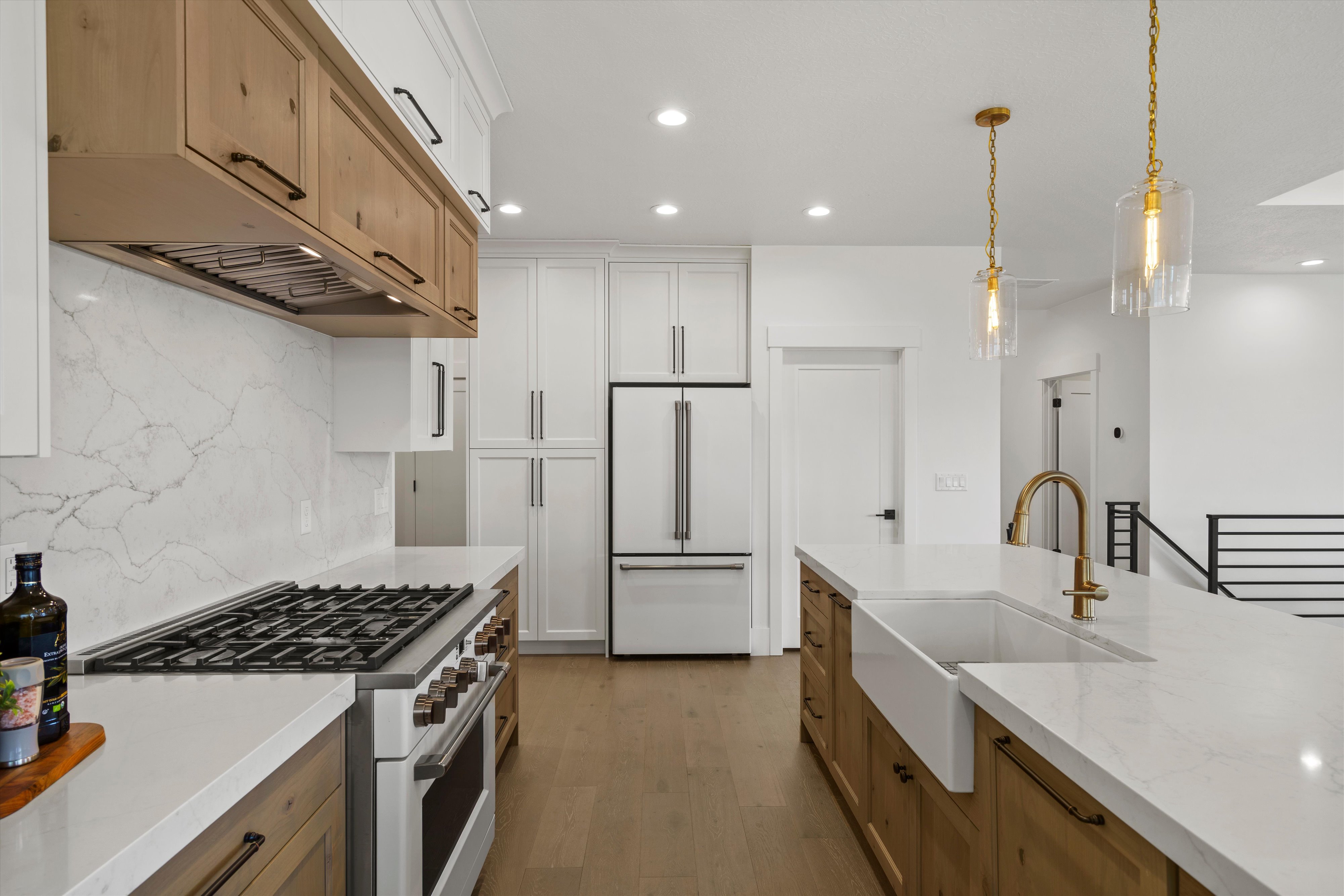 Dual tone kitchen with dual tone cabinets, high end appliances, light stone countertops, light wood-style floors, and decorative backsplash