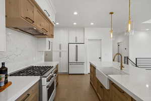 Dual tone kitchen with dual tone cabinets, high end appliances, light stone countertops, light wood-style floors, and decorative backsplash