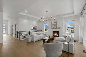 Living room with suspended lighting, healthy amount of natural light, a tray ceiling, light wood finished floors, and a glass covered fireplace