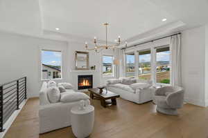 Living area featuring a chandelier, a raised ceiling, light wood-type flooring, plenty of natural light, and a glass covered fireplace