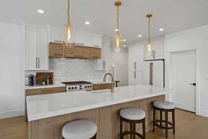 Kitchen with light wood-style flooring, dual tone cabinets, a large island, and hanging light fixtures