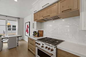 Kitchen with high end range, tasteful backsplash, light wood-style flooring, light stone counters, and recessed lighting