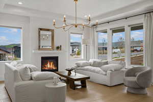 Living room with light wood-style flooring, hanging lights, a glass covered fireplace, and a raised ceiling