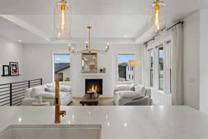Kitchen with open floor plan, suspended lighting, wood finished floors, a tray ceiling, and a warm lit fireplace