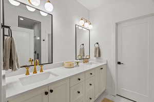 Bathroom featuring double vanity, light marble finish flooring, and a stall shower