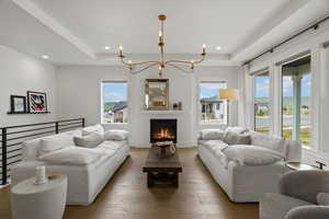 Living area featuring hanging lights, a raised ceiling, hardwood / wood-style flooring, and a lit fireplace