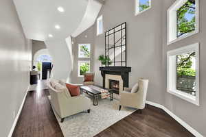Living area with a warm lit fireplace, dark wood-type flooring, a high ceiling, and recessed lighting