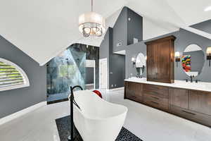 Bathroom with vaulted ceiling, a marble finish shower, double vanity, a chandelier, and a freestanding tub