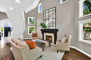 Living room with a high ceiling, a warm lit fireplace, dark wood finished floors, and recessed lighting