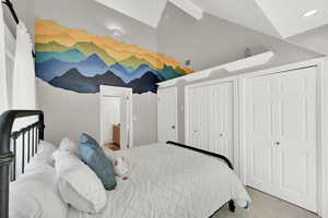 Bedroom featuring light carpet, lofted ceiling, two closets, and ensuite bath