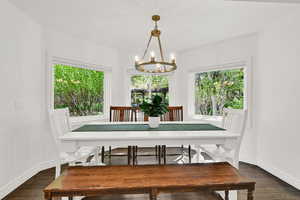 Dining space with dark wood finished floors, hanging lights, and plenty of natural light