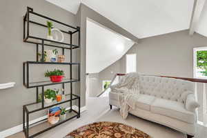 Carpeted living area with lofted ceiling with beams and baseboards