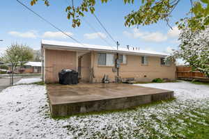 Snow covered house featuring a gate, brick siding, and a patio area