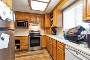 Kitchen featuring stainless steel appliances, wood finish cabinets, light countertops, open shelves, and healthy amount of natural light
