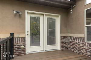 Property entrance with stucco siding, a deck, and brick siding