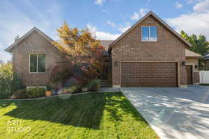 Traditional-style house with a front lawn, concrete driveway, brick siding, and an attached garage