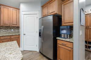 Kitchen with stainless steel refrigerator with ice dispenser, backsplash, wood finish cabinets, and light wood-style flooring