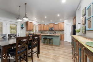 Kitchen with light wood-type flooring, a kitchen island, decorative light fixtures, tasteful backsplash, and two tone cabinets