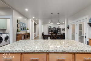 Kitchen with light stone countertops, open floor plan, washer and dryer, hanging light fixtures, and a kitchen island